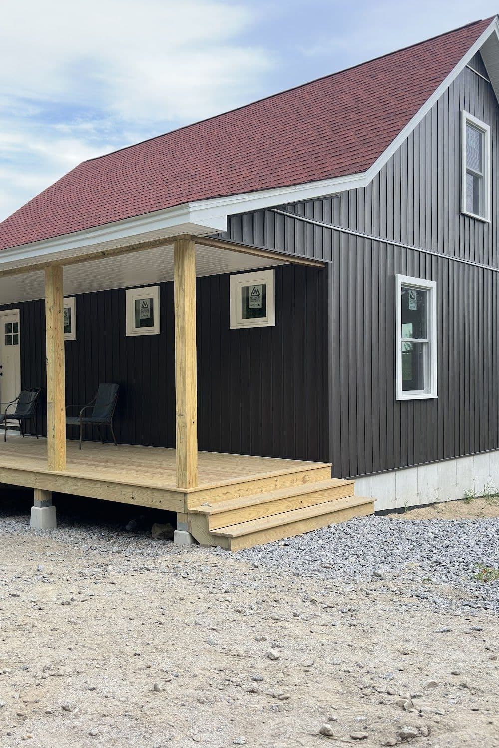 Charcoal board and batten cabin with a red roof and covered porch, sided by Wolf's Siding in Washington, NH